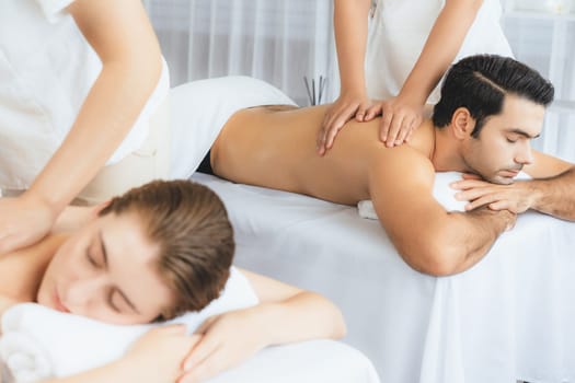 Caucasian couple customer enjoying relaxing anti-stress spa massage and pampering with beauty skin recreation leisure in day light ambient salon spa at luxury resort or hotel. Quiescent