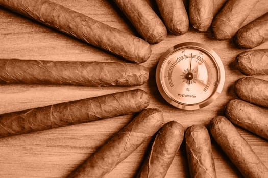 Cigars with humidor hygrometer on the wooden background. Image toned in Peach Fuzz color of the year 2024