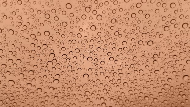 Abstract image of rain drops on glass. Image toned in Peach Fuzz color of the year 2024. New Fashion color. Top view. Abstract drops view