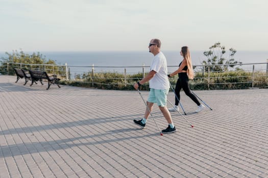 Happy Middle aged couple or friends practicing nordic walking in park near sea. Mature couple with trekking poles walking, practicing Nordic walking outdoors. Aging youthfully and sport concept.