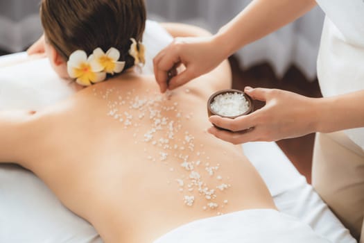 Woman customer having exfoliation treatment in luxury spa salon with warmth candle light ambient. Salt scrub beauty treatment in health spa body scrub. Quiescent