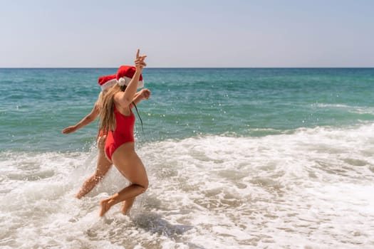 Women in Santa Claus hats run into the sea dressed in red swimsuits. Celebrating the New Year in a hot country.