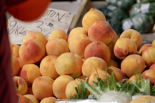 pile of peaches on a table in a street market with a price sign