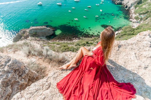 Woman red dress sea. Happy woman in a red dress and white bikini sitting on a rocky outcrop, gazing out at the sea with boats and yachts in the background