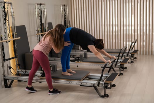 Overweight caucasian woman doing pilates exercises on reformer with personal trainer