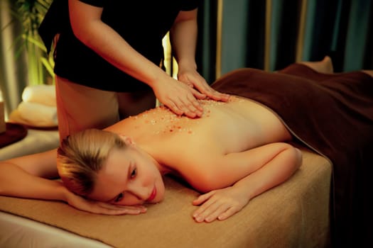 Woman customer having exfoliation treatment in luxury spa salon with warmth candle light ambient. Salt scrub beauty treatment in Health spa body scrub. Quiescent