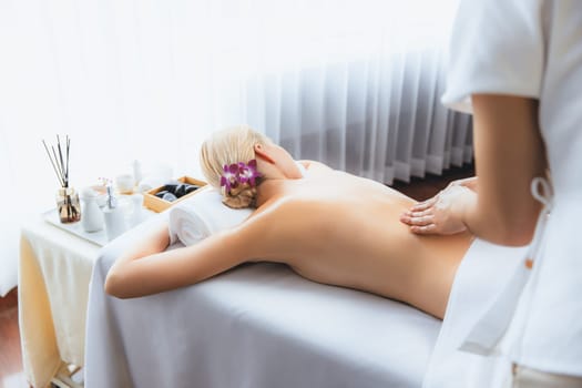 Caucasian woman customer enjoying relaxing anti-stress spa massage and pampering with beauty skin recreation leisure in day light ambient salon spa at luxury resort or hotel. Quiescent