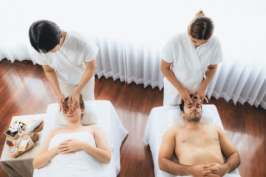Caucasian couple enjoying relaxing anti-stress head massage and pampering facial beauty skin recreation leisure in dayspa modern light ambient at luxury resort or hotel spa salon. Quiescent