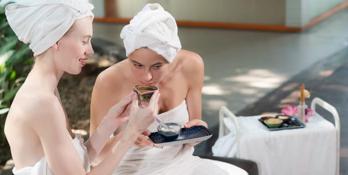 Couple of beautiful woman interested in homemade facial masks while sitting at spa salon. Attractive woman in white towel enjoy herbal masks with her friend surrounded by nature. Tranquility.