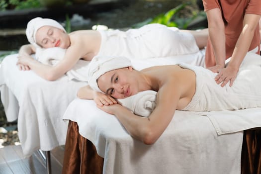 A portrait of two young attractive woman lie on bed during having back massage by a professional masseur at outdoor surrounded by peaceful natural environment. Healthy and beauty concept. Tranquility.