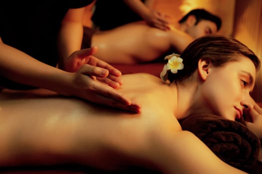 Caucasian couple customer enjoying relaxing anti-stress spa massage and pampering with beauty skin recreation leisure in warm candle lighting ambient salon spa at luxury resort or hotel. Quiescent