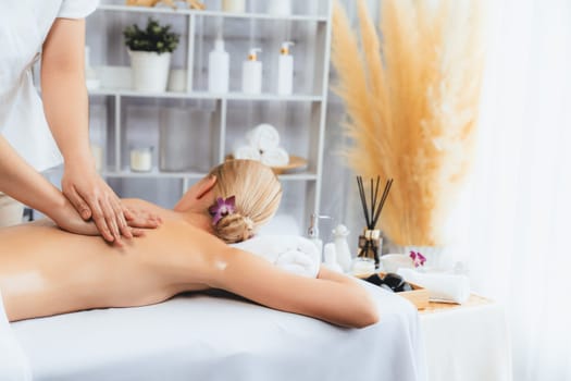 Caucasian woman customer enjoying relaxing anti-stress spa massage and pampering with beauty skin recreation leisure in day light ambient salon spa at luxury resort or hotel. Quiescent