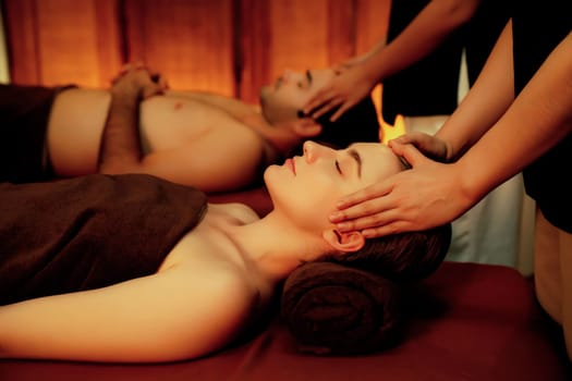 Couple customer enjoying relaxing anti-stress head massage and pampering facial beauty skin recreation leisure in warm candle lighting ambient salon spa in luxury resort or hotel. Quiescent