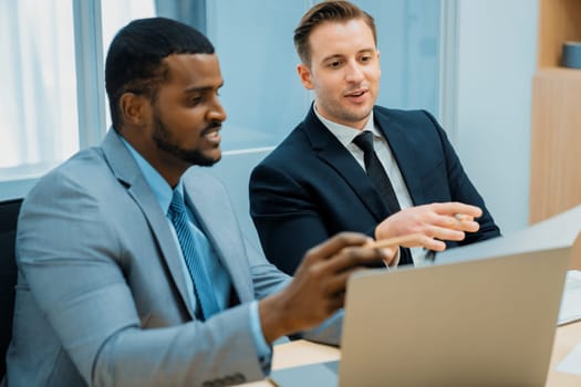 African male leader explain strategy while show solution to professional project manager by pointing at document, using laptop. Skilled business team brainstorming idea. Business meeting. Ornamented.