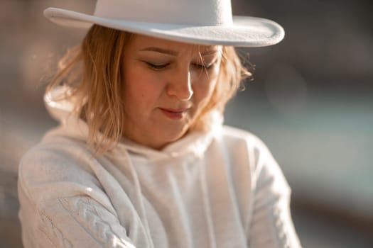 Happy blonde woman in a white suit and hat posing at the camera against the backdrop of the sea.