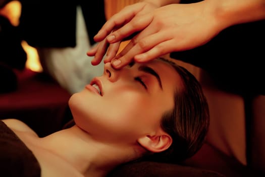 Caucasian woman enjoying relaxing anti-stress head massage and pampering facial beauty skin recreation leisure in warm candle lighting ambient salon spa in luxury resort or hotel. Quiescent
