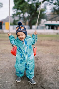 Little smiling girl trying to sit on the swing holding on to the ropes. High quality photo