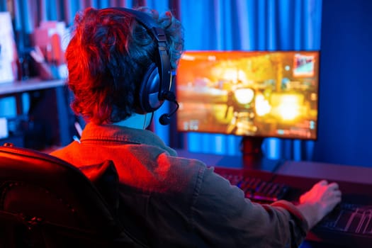 Host channel of young gaming streamer, team gamer playing battle game shooting with multiplayer at warship on pc screen with back side image, wearing headset with mic at digital neon room. Gusher.