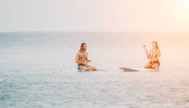 Sea woman and man on sup. Silhouette of happy young woman and man, surfing on SUP board, confident paddling through water surface. Idyllic sunset. Active lifestyle at sea or river