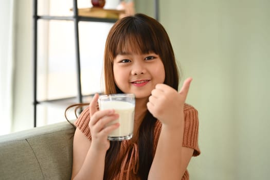 Happy Asian child holding a glass of milk and showing thumb up. Growth and nutrition concept