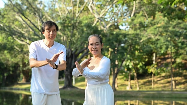 Happy mature people practicing traditional Tai Chi Chuan outdoor near lake at sunset in summer park.