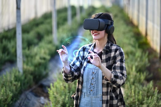 Female farmer wearing VR glasses standing in greenhouse. Innovative and smart farming concept