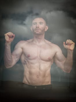 A Muscular Shirtless Red-Haired Man Looking out of the Window in a Cloudy Day