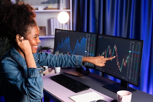 African woman blogger exited with happy face, pointing on screen with valued stock market achievement at high profit. Concept of exchange investment online in trading application on pc. Tastemaker.
