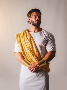 A muscular man with a beard wearing a yellow scarf and white robe, in a Greek or Roman god costume, in studio shot
