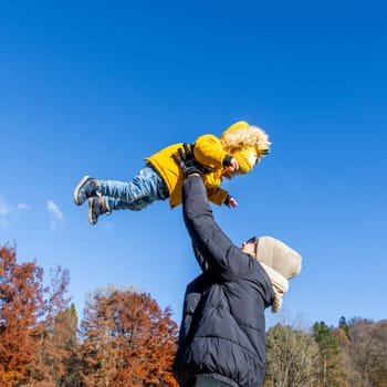 More, more,...mum, that's fun. Happy young mother throws her cute little baby boy up in the air. Mother's Day, Mather and her son baby boy playing and hugging outdoors in nature in fall