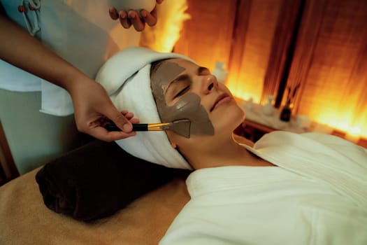 Serene ambiance of spa salon, woman customer indulges in rejuvenating with charcoal face cream massage with warm lighting candle. Facial skin treatment and beauty care concept. Quiescent