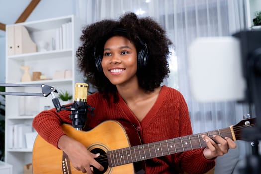 Host channel of beautiful African woman influencer singing with playing guitar in broadcast studio on smartphone. Time slot of music blogger on live social media. Concept of audio creator. Tastemaker.