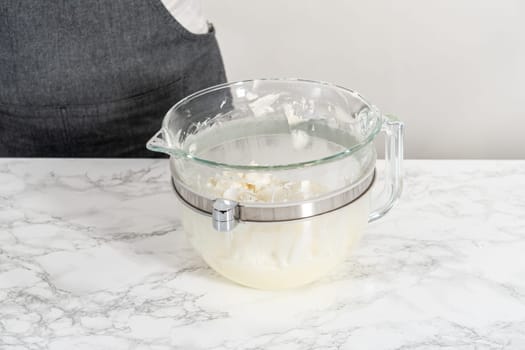 Whisking buttercream frosting in a glass mixing bowl with an electric kitchen mixer for American flag mini cupcakes.