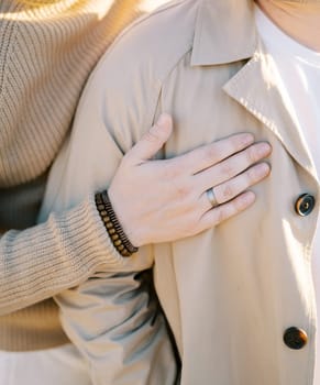 Man hugs his partner from behind with his hand on his chest. Cropped. Faceless. High quality photo