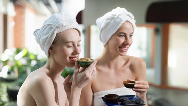 Couple of beautiful woman interested in homemade facial masks while sitting at spa salon. Attractive woman in white towel enjoy herbal masks with her friend surrounded by nature. Tranquility.