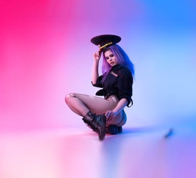 Sexy girl in police uniform posing in underwear with a police rubber baton in neon light on an empty background