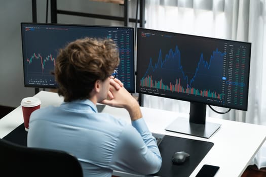 Working young business trader focusing on market stock dynamic graph data in real time two pc screens with back side at modern office. Concept of analyzing dynamic financial exchange rate. Gusher.