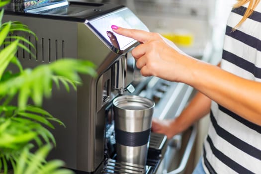 A young woman makes fresh flavored coffee with a modern coffee machine in her kitchen.