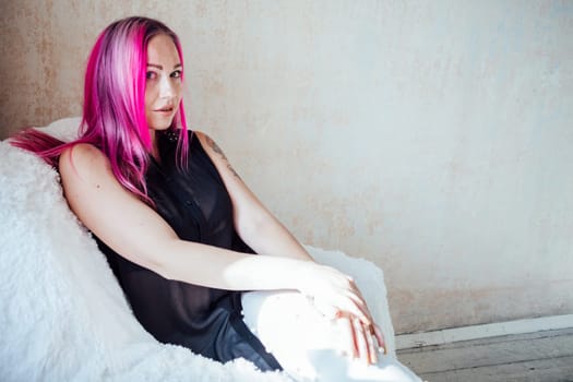 girl with pink hair sits in a Chair in a white room 1
