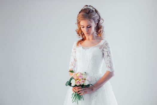 bride in wedding dress with a bouquet of flowers in a white room