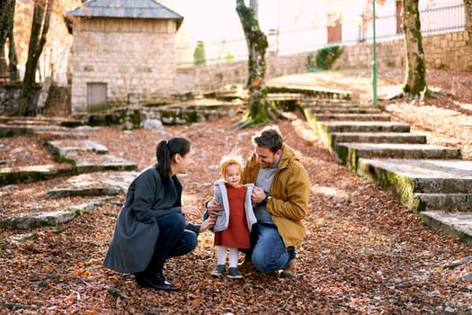 Dad hugs a little girl standing next to him with mom squatting in the forest. High quality photo