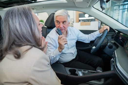 Mature Caucasian couple sitting in a new car and rejoicing at the purchase