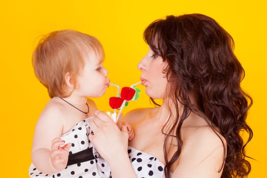 mother and little daughter drunk from drinking straws cocktail on a yellow background