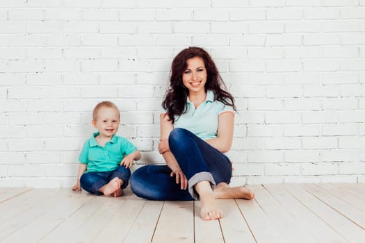 mom and young boy son sit on the floor white brick wall