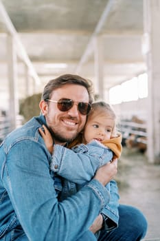 Smiling dad hugging little girl while squatting by corral. High quality photo