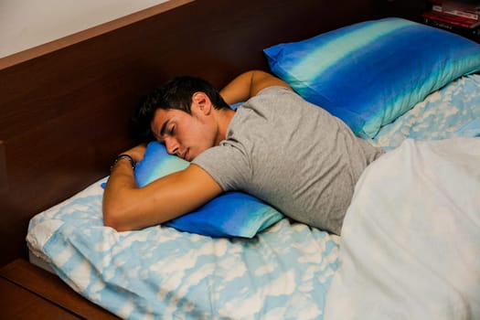 A man laying on a bed with a pillow. Photo of a handsome young man resting on a comfortable bed with a soft pillow