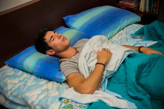 A man laying on a bed with a pillow. Photo of a handsome young man resting on a comfortable bed with a soft pillow