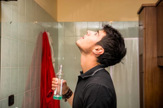 Head and Shoulders Close Up of Attractive Young Man with Dark Hair Rinsing with Mouth Wash in Bathroom as part of Morning Grooming Routine