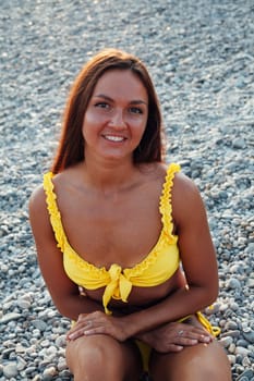 woman with long hair in a yellow swimsuit walks on the beach by the sea