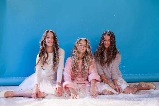 Three beautiful fashionable girl girlfriends in a winter snow cap blue background